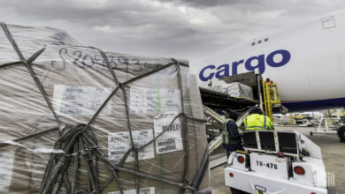 Close up photo of a shrink-wrapped pallet on the tarmac waiting to be loaded in the cargo door of a large aircraft.