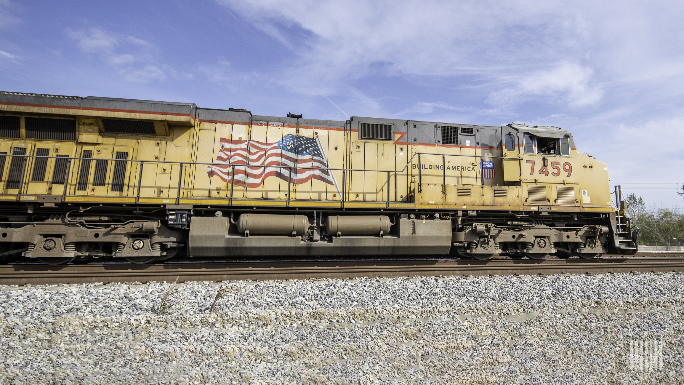 A yellow Union Pacific locomotive travels along train tracks with a blue sky in the background.