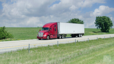 A maroon tractor pulling a white trailer on a highway