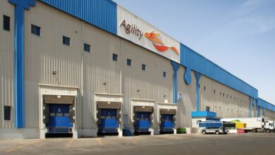 A warehouse with Agility logo on it, blue truck docks and trim around the roof, seen on a bright sunny day.