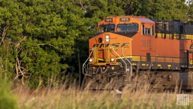 A locomotive with the letters BNSF painted on its front passes by a forest.