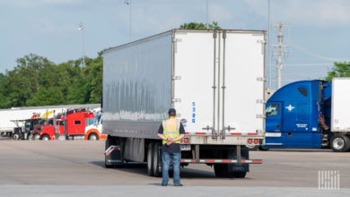 Truck driver trainer stands behind truck backing up