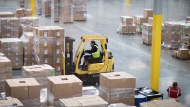 A yellow forklift operates around stacks of boxes in a warehouse.