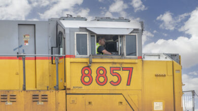 A man sits inside a freight train locomotive.