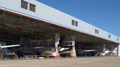 View of giant aircraft hangar with several aircraft inside, viewed from outside the entrance on a sunny day.