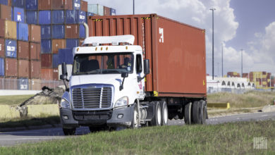 A white truck pulling a red ocean container at the Port of Houston