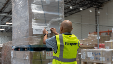 Picture from behind a man in a yellow vest with Flexport label working in a warehouse.
